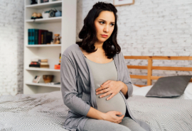 Embarazada sentada en la cama con gesto de duda